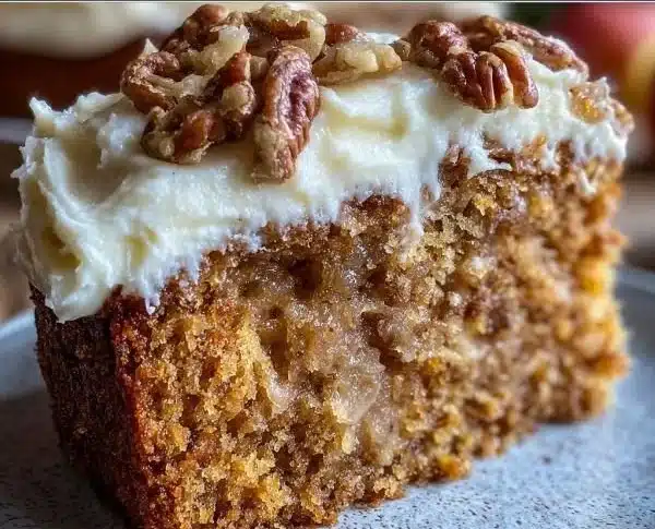 A slice of fresh apple cake with cream cheese frosting on a white plate