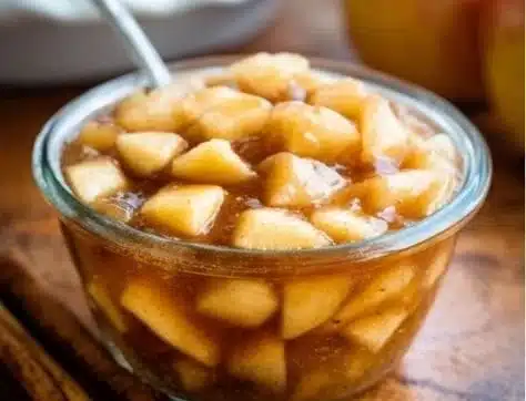 Homemade apple pie filling in a glass bowl with fresh apples and spices.