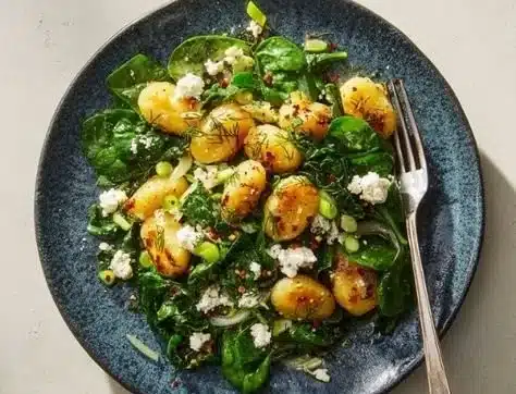 Plate of gnocchi with spinach and feta cheese garnished with herbs